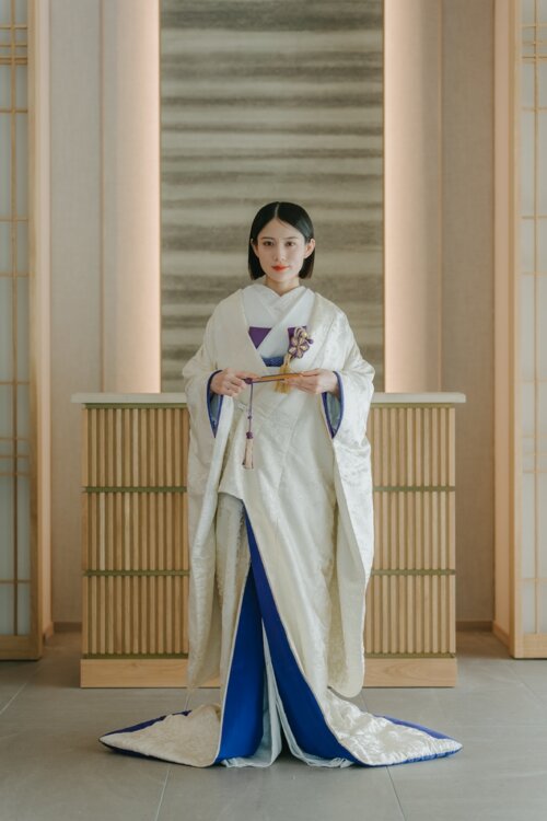 Full-length shot of a bride in a shiromuku holding a folding fan in a modern Japanese-style studio, the blue under-kimono and hem trim adding color to this pre-wedding photoshoot in Japan (Shiromuku AR102).