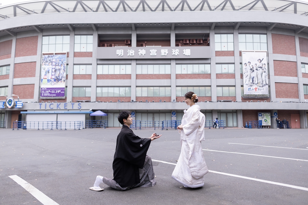 Groom kneeling to propose to the bride in shiromuku in front of Jingu Stadium in Tokyo, a personal kimono wedding photo