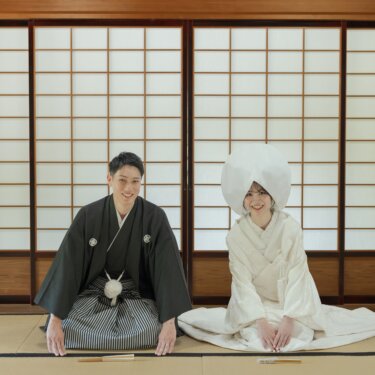 Groom in montsuki and bride in shiromuku with a wataboshi hood kneeling on tatami in front of shoji screens at Daisen Park Japanese Garden, a formal seated pose for kimono wedding photos