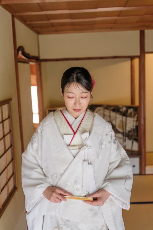 Bride in a shiromuku with silver embroidery holding a fan and lowering her eyes in a tatami room, kimono wedding photos in Japan (SR102)