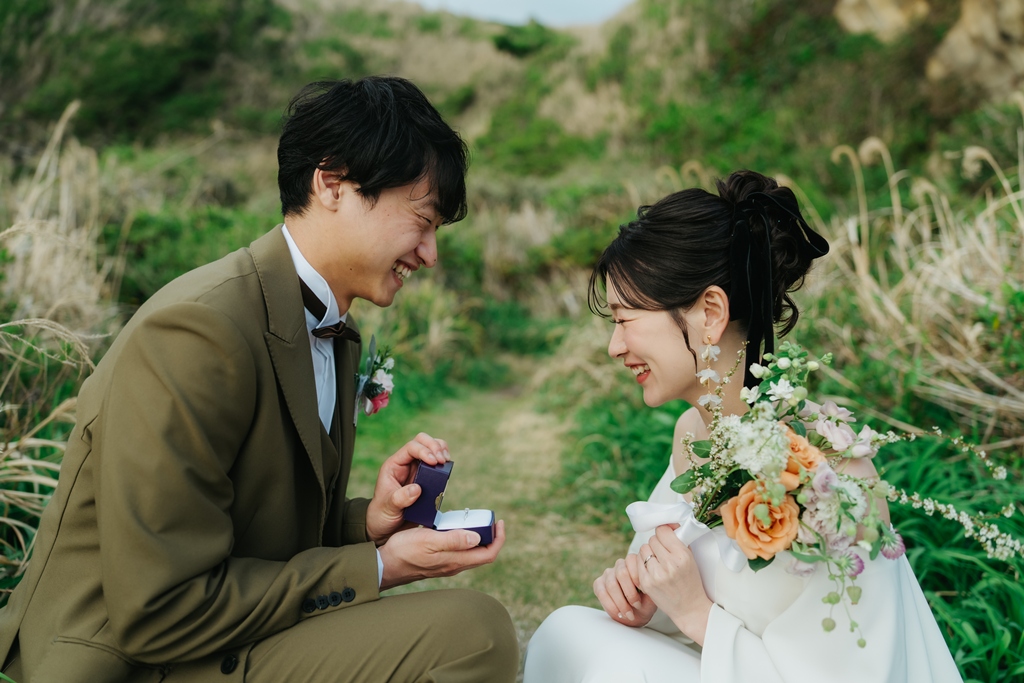 Groom opening a ring box to propose to the bride in a grassy field on Jogashima, proposal recreation wedding photo