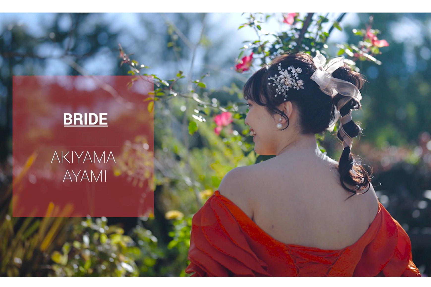 Video still reading 'BRIDE AKIYAMA AYAMI', bride in a vivid orange gown glancing over her bare shoulder amid rose blossoms.