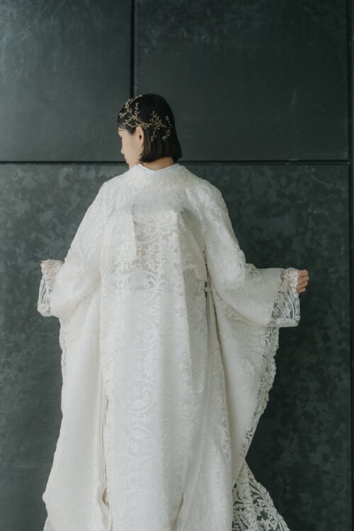 Bride spreading both sleeves to show the pattern on the back of her shiromuku, a gold branch headpiece completing this Japan wedding photography shot (DE101).