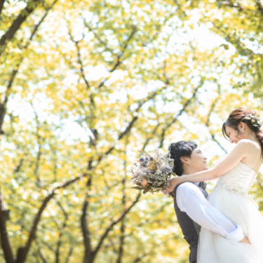 Groom lifting the bride in a wedding dress with a dried flower bouquet under yellow autumn trees, a joyful autumn pre-wedding photoshoot in Japan