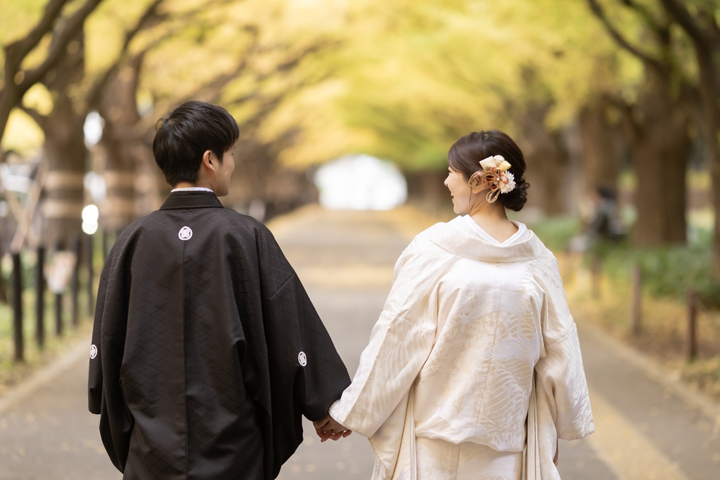 Kimono couple walking hand in hand along the ginkgo-lined sidewalk at Jingu Gaien, seen from behind