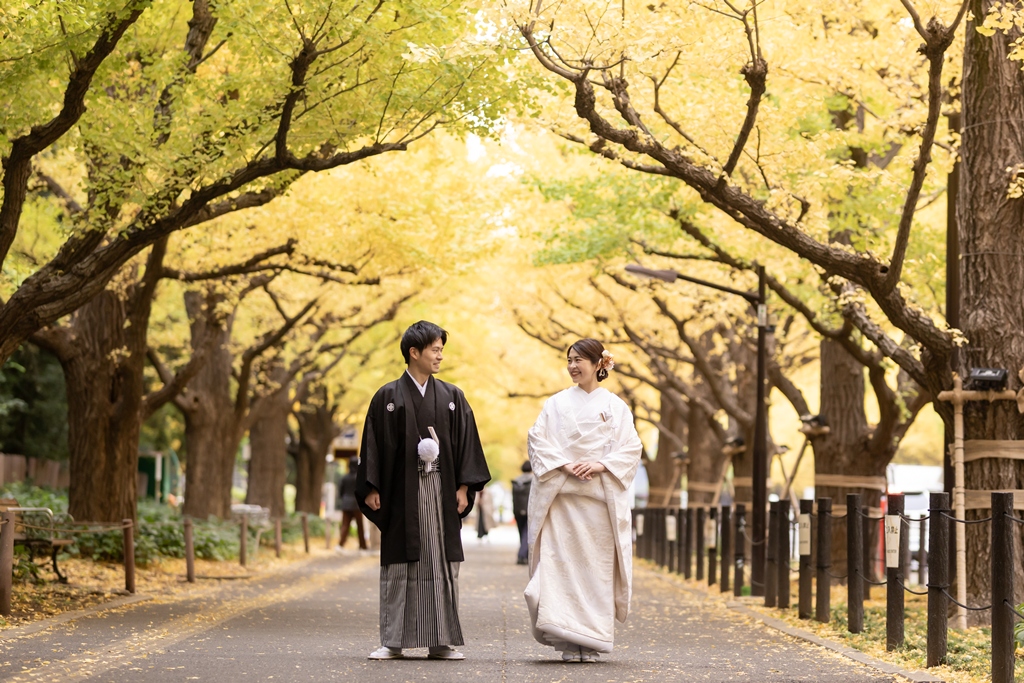 Bride in white shiromuku and groom in montsuki hakama walking under the golden ginkgo trees of Jingu Gaien, autumn kimono wedding photos in Tokyo