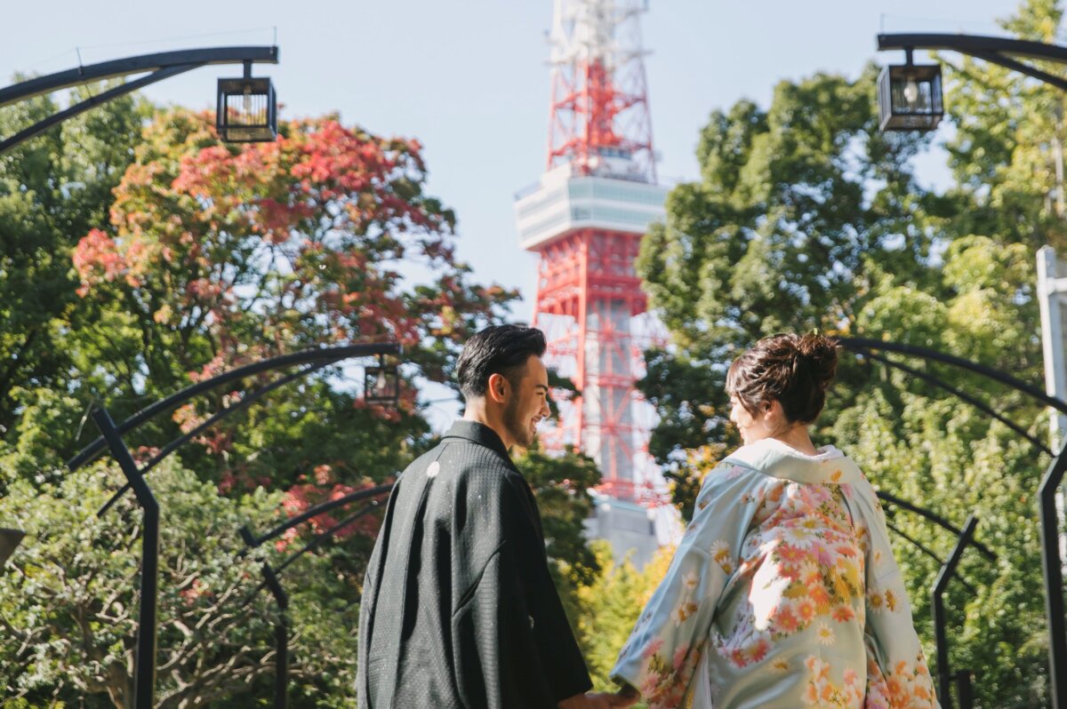 Kimono couple facing each other on a park path with autumn trees and Tokyo Tower in the background, pre-wedding photoshoot in Japan