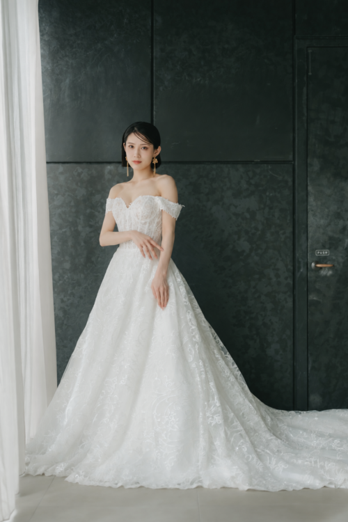 Bride with arms lightly crossed against a dark wall in the floral lace DC02 wedding dress with a full skirt, a studio pre-wedding photoshoot in Japan