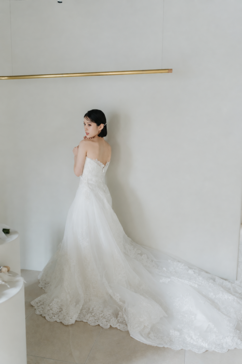 Bride showing her back and glancing over her shoulder in a long-train wedding dress with lace at the hem, a back view pose for a pre-wedding photoshoot in Japan